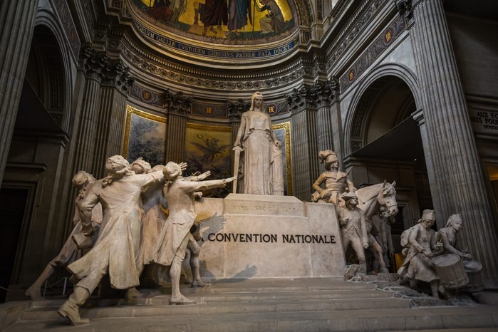 A large marble statue of a woman, surrounded by a crowd of men