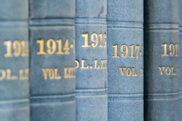 A line of light blue book spines with gold words on them, each with a year and volume number on them