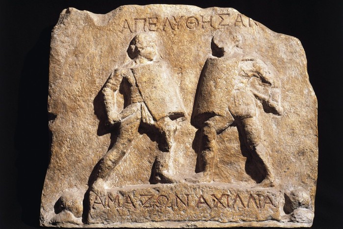 This marble relief from Halicarnassus, dating to the 1st–2nd centuries AD, commemorates the honourable discharge of two female gladiators known as “Amazon” and “Achillia.” Shown armed like their male counterparts but bareheaded to reveal their hairstyles, the pair exemplifies the rare but striking presence of women in the arena — a reminder of the diversity and spectacle that characterised Roman gladiatorial combat.