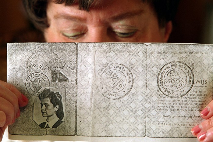 A woman holds up an old passport in front of her face. On the left page there is a black and white photo of a young girl