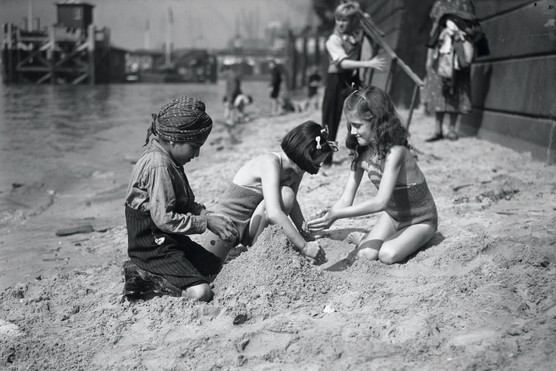 A black and white photograph showing a young boy playing with two girls in the sand