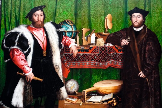 Two men dressed in Tudor clothes stand next to one another against a green curtain backdrop. Between them are several items, including a globe, a hymnbook and a lute